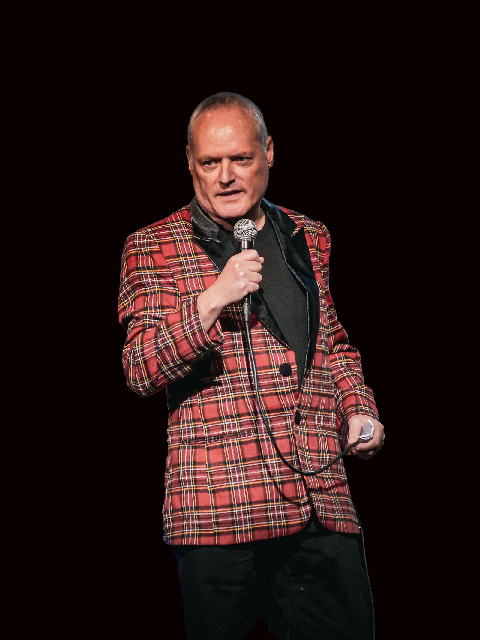Mark Docherty, Scottish actor and stand-up comedian, on stage in his red tartan jacket holding a microphone